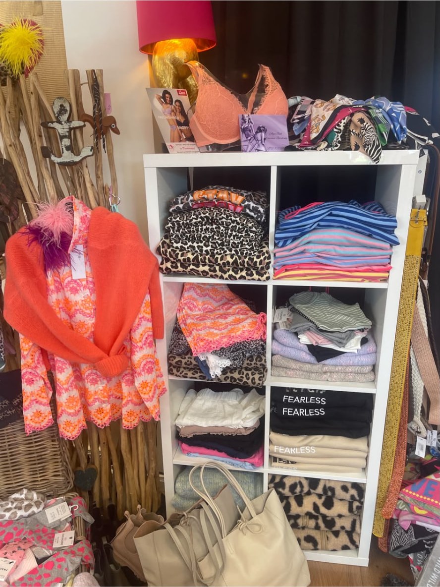 Regal mit Tüchern, Taschen und Accessoires neben einer pinken Lampe